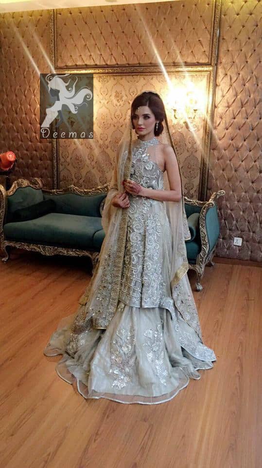 This outfit is a timeless beauty. It is heavily embellished with silver kora, dabka, sequins and swaronski crystals. This exquisite A-line frock is fully decorated with floral motifs patterns all over it. It is further enhanced with halter neckline.It comes with sharara which has small sized sprinkled floral motifs all over. This Outfit is beautifully coordinated with matching dupatta with heavy embroidered borders and finished with piping.