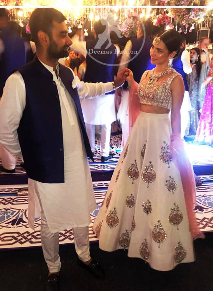 The blouse is beautifully embellished with cutwork embroidery enhanced with silver gold kora dabka, kundan and sequins work. It is paired up with ivory lehenga with colorful pattern embellishment ornamented with kora dabka, and colorful thread embroidery. It comprises with peach dupatta sprinkled sequins all over.