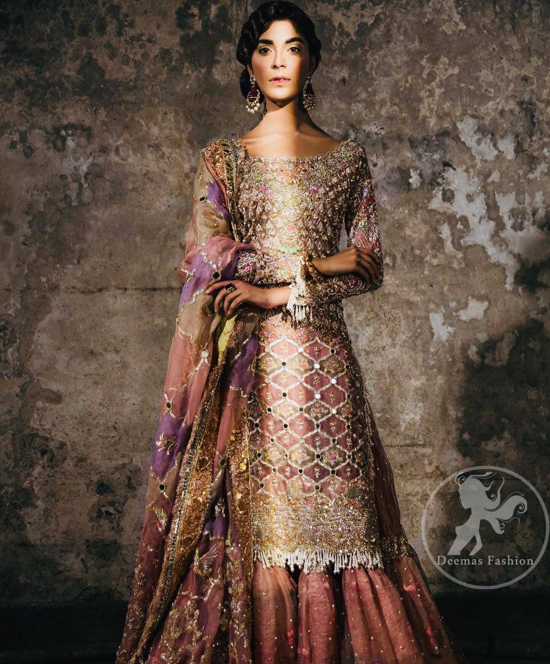 This bridal dress stands out due to its uniqueness and the perfect fusion of modern cut and traditional embroidery. It is enhanced with kora, dabka, tilla, gota, sequins and pearls. Shirt is fully embellished in crisscross pattern. It is artistically coordinated with tissue gharara which is adorned with colourful motifs and colourful embroidered dupatta detailed with gold gota work and finishing adds to the look.