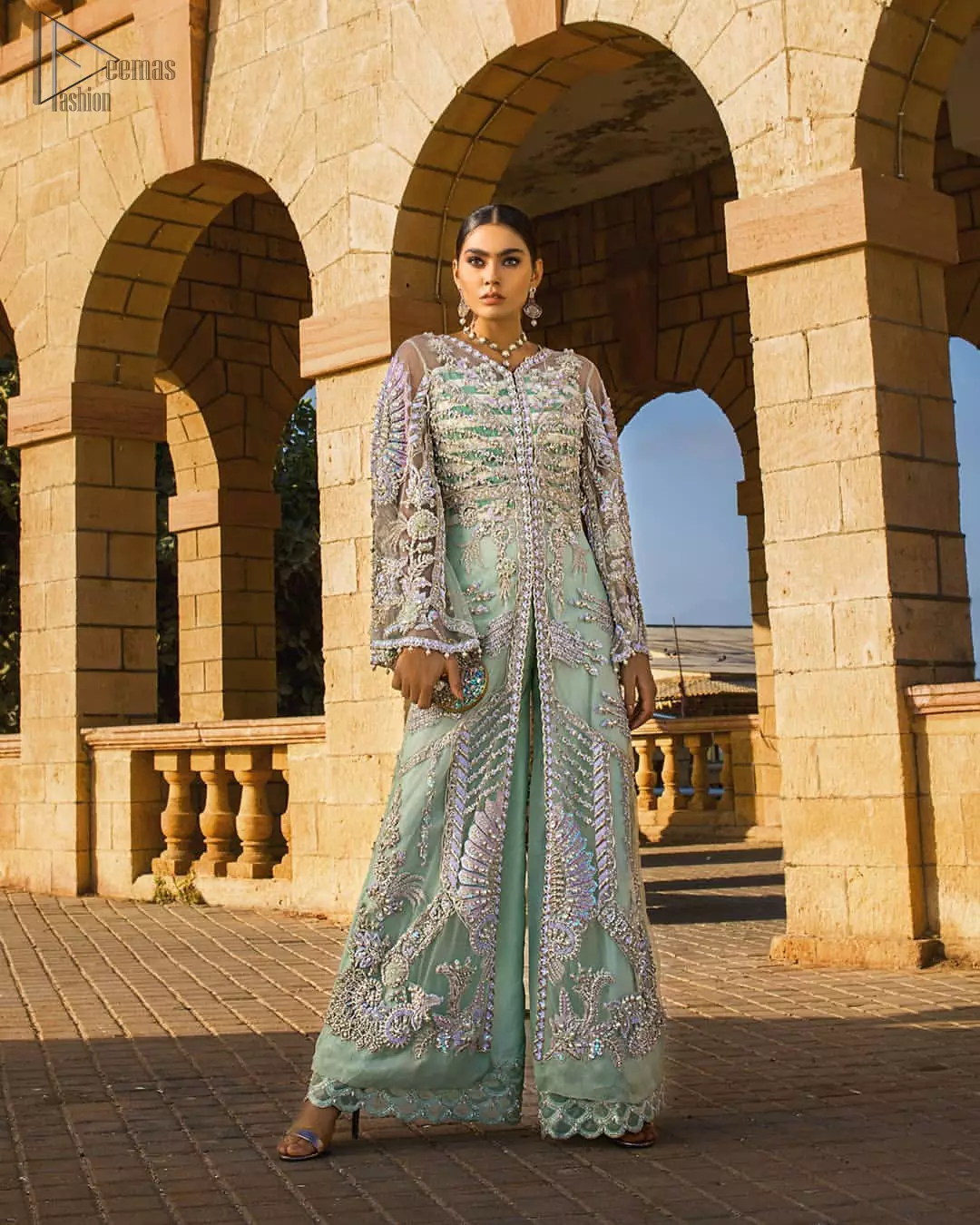 Take a step towards refreshing your wardrobe with aqua front open gown and palazzo pants. This front open gown is perfected with loaded light golden and silver work. The front of the gown is heavily embellished with different styles motifs and rich embellishment on bodice. Furthermore the back of the gown and bell sleeves are also decorated with detailed embroidery and dangling balls. The palazzo pants with it is made of raw silk fabric with lace detail on the bottom. The outfit is coordinated with aqua organza dupatta sprinkled with sequins all over.