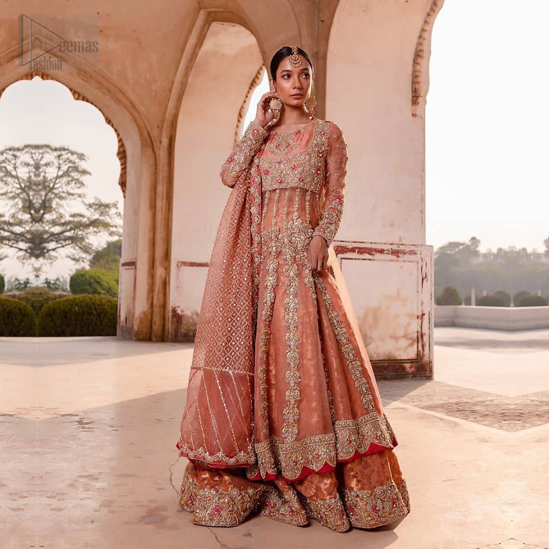 You are all set to make a lasting impact with the divine royalty of this dress. This garment is sure to make you look like glamorous with immaculate work covering every inch of the pishwas with multiple panels. This pishwas made of zardozi work with scalloped hemline and applique is everything that you need for your festivities. The brocade lehenga is beautifully adorned with thick embellished bottom with zardozi work in the shades of silver and gold. Style it up with peach organza dupatta with criss-cross patterns and floral booties on borders. This is an ensemble that deserves to be flaunted.
