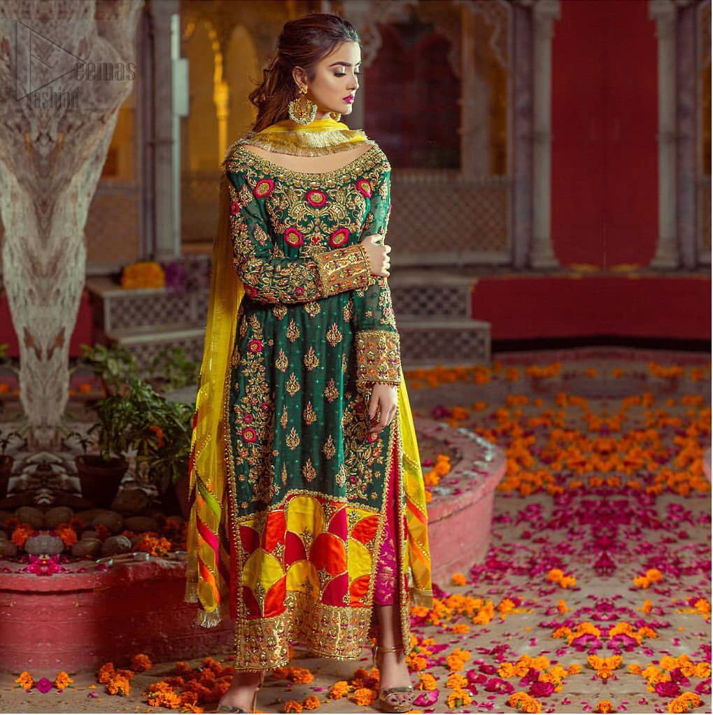 Beautifully elegant with a modern twist. This beautiful outfit comes with bottle green long shirt and colorful applique hemline, making an elegant, traditional and stylish mehndi dress. Excellence of craftsmanship is evident with intricate geometrical detailing that features the use of kora, dabka, crystals, sequins and glass beading. Furthermore it is enhanced with colorful floral motifs and golden zardozi work. It comprises with pink capri pants. Elegance is personified when it gets paired up with net dupatta with kiran on all sides and colorful strips on pallu.