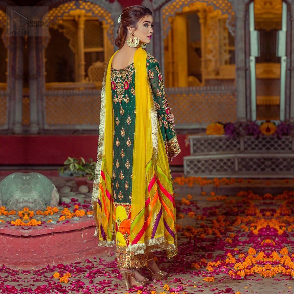 Beautifully elegant with a modern twist. This beautiful outfit comes with bottle green long shirt and colorful applique hemline, making an elegant, traditional and stylish mehndi dress. Excellence of craftsmanship is evident with intricate geometrical detailing that features the use of kora, dabka, crystals, sequins and glass beading. Furthermore it is enhanced with colorful floral motifs and golden zardozi work. It comprises with pink capri pants. Elegance is personified when it gets paired up with net dupatta with kiran on all sides and colorful strips on pallu.