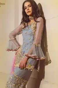Gray Short Shirt Sharara – Pink Dupatta. The chic yet elegant outfit is decorated with golden embroidery, an embellished neckline, and tiny floral motifs. Borders are even more enhanced with golden zardozi detailed patterns and finished with scallops and dangling balls. Pair it with gray sharara highlighted with floral jaal and scalloped bottom with golden kora, dabka, and tilla work.