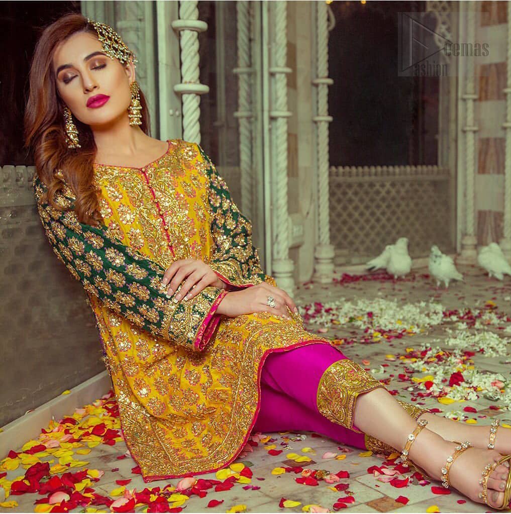 Embrace the season of festivities with this beautiful dress. This beautiful mehndi dress comes with a pink capri pants with beautiful embellished applique around the bottom and the shirt is designed with vertically worked gold lines and it finished with a thick appliqued embellished border. The shirt looks more whimsical when it comes with embellished green sleeves with golden zardozi work. Balance the look with yellow organza dupatta scattered with sequins on the ground.