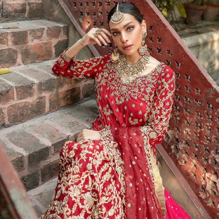It’s ALL in the details, This breathtaking wedding dress offers comfort without compromising on style. This outfit laden with ornamental embellishments and embroidery creates such a fairytale touch to your big day. Paired with a pink sharara creates an unusual charisma wholeheartedly. Embroidery is done in the shade of golden and tiny floral motifs scattered all over the shirt. Sharara is emphasized with sequins spray and zardozi details at the bottom. Complete the look with a red dupatta having scalloped borders and scattered tiny floral motifs all over the ground.