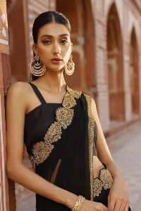 Every saree tells a story! Black is always the reason behind any smile at parties. DeemasFashion also presents a formal saree in black that you can wear at any function or party. The black blouse having sleeveless and strap neckline gives you so soothing and romantic look. Further, the simplicity of the blouse enhances the beauty of the outfit. It comes with a pure black saree which is ornamented with golden embroidery. It is highlighted with tilla, kora, and dabka work on borders. The pallu of the saree is also prominent with golden embridery. 